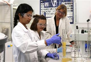 Kolme naista valkoisissa takeisessa työskentelemässä laboratoriossa.