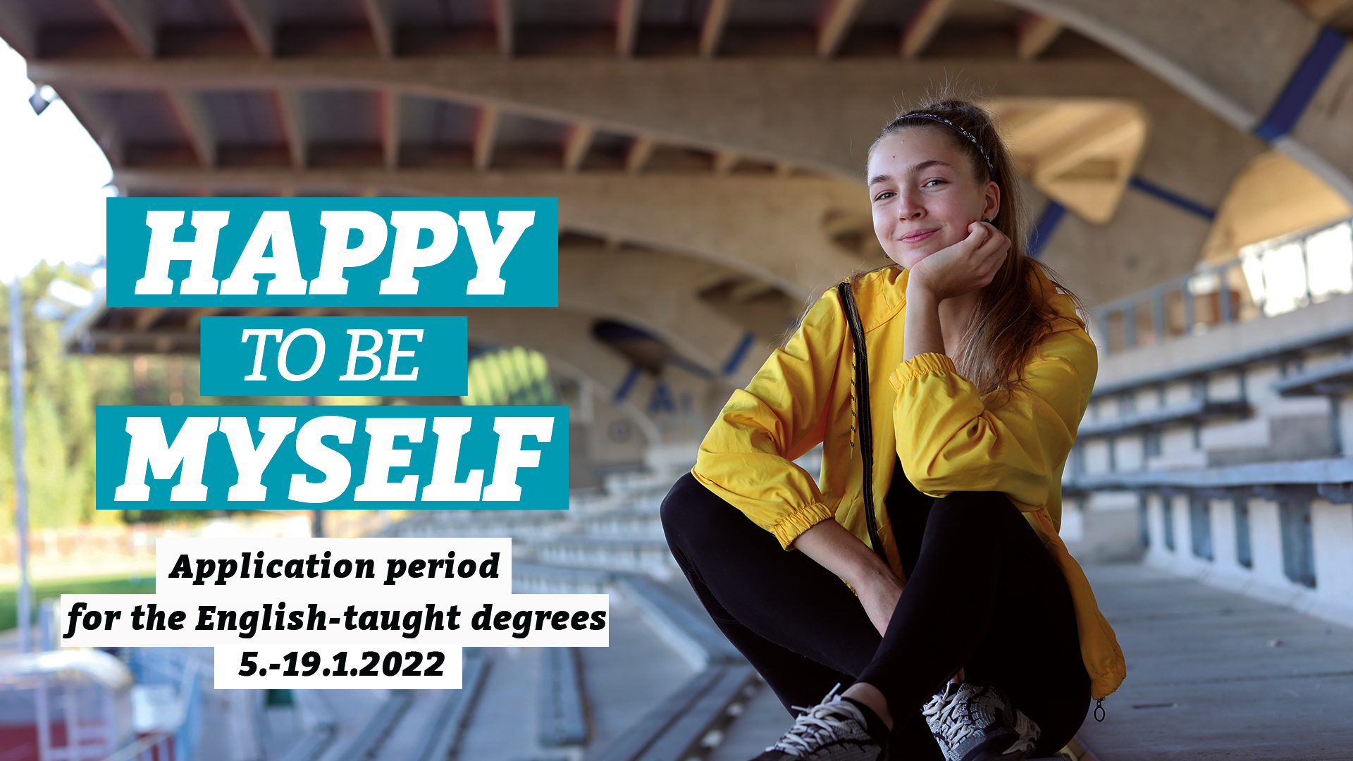 A girl with a yellow jacket is sitting on the sports auditorium.The picture shows the text happy to be myself.