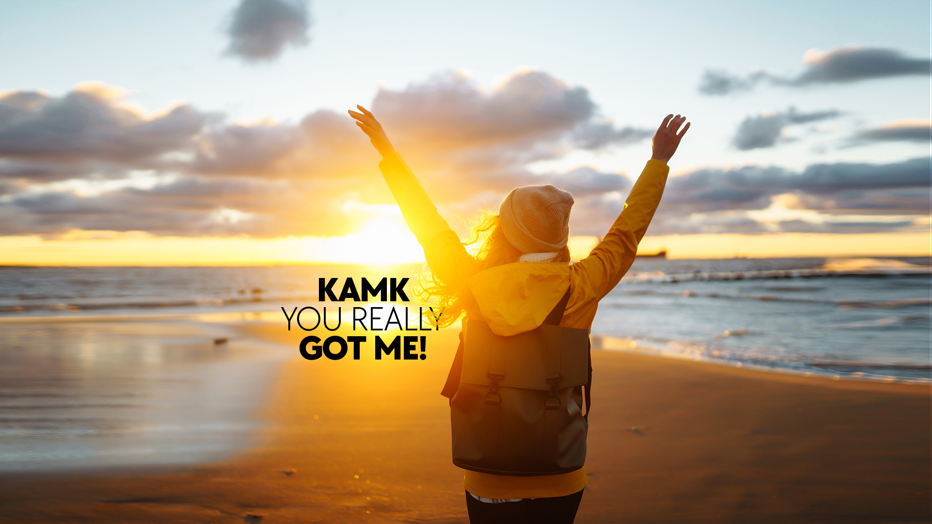 The girl is standing on the beach, looking out to sea with her hands up. The picture says KAMK you really got me.